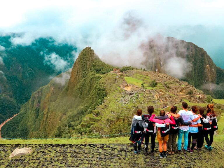 Un groupe de voyageurs WeRoad de dos contemple les ruines antiques de Machu Picchu au Pérou sous un ciel brumeux.