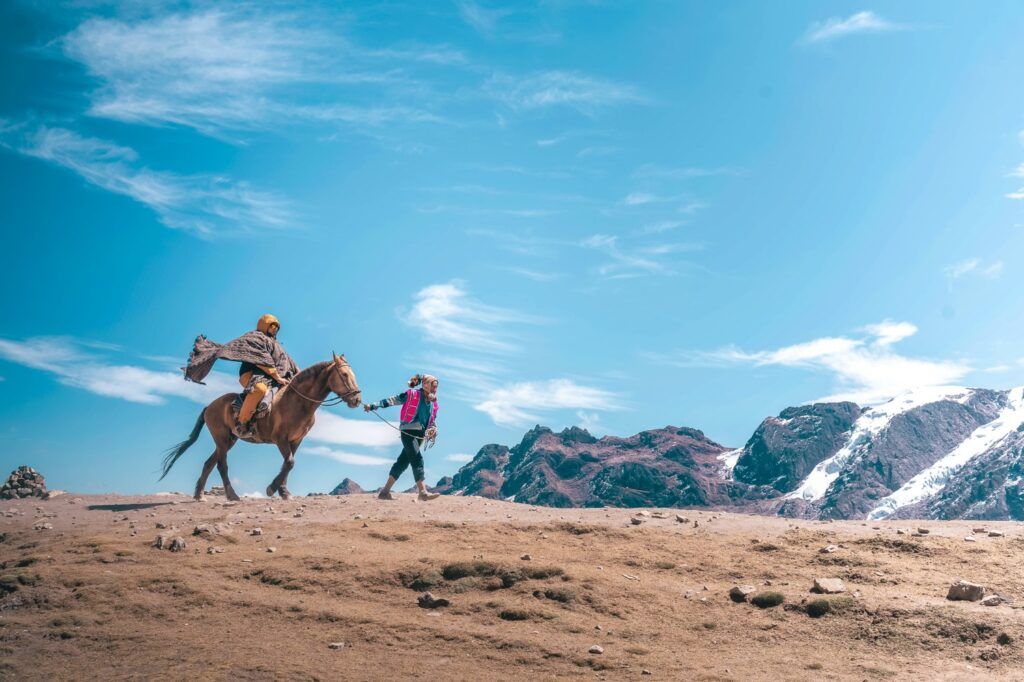 Un voyageur à cheval guidé par une personne locale sur un sentier de haute montagne dans les Andes péruviennes.