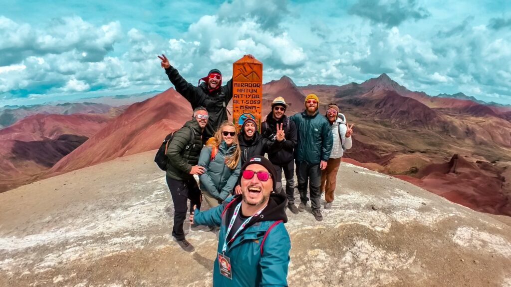 Un groupe de voyageurs WeRoad pose au sommet du Mirador Hatun Rit'iyoc au Pérou, avec les montagnes colorées en arrière-plan.