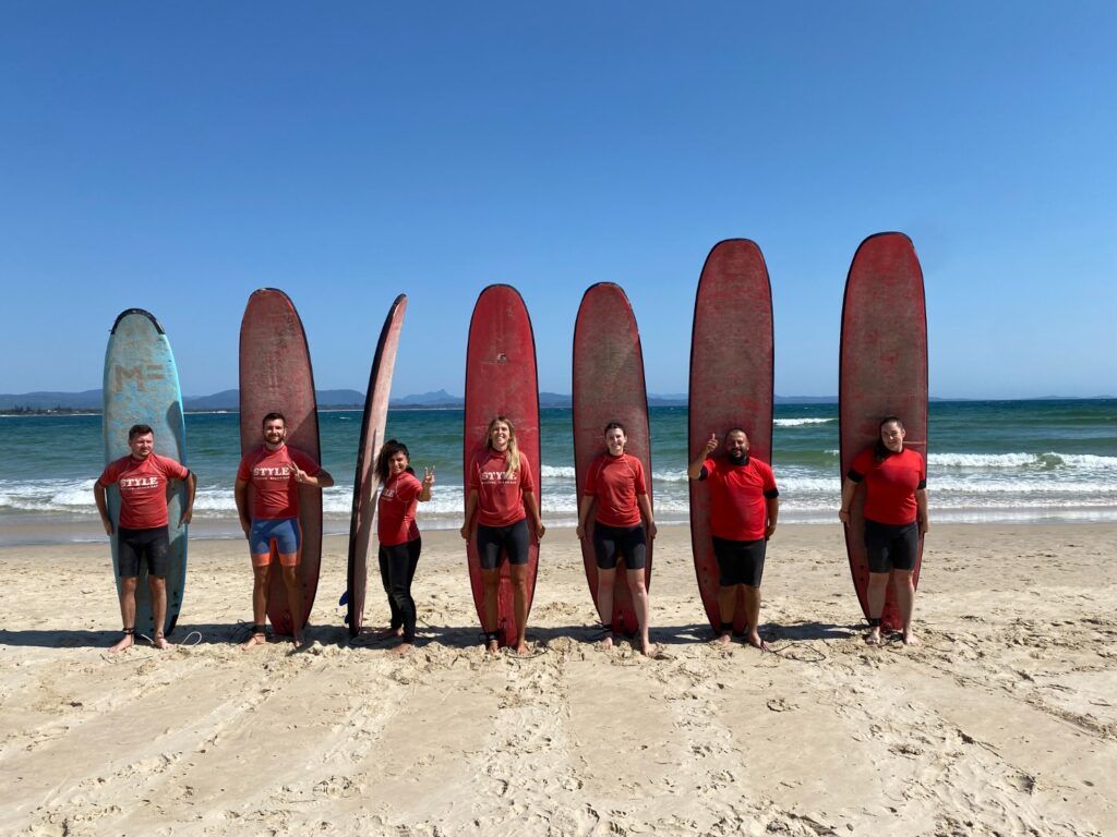 Un groupe de voyageurs WeRoad posant debout sur une plage avec leurs planches de surf à Byron Bay, en Australie.