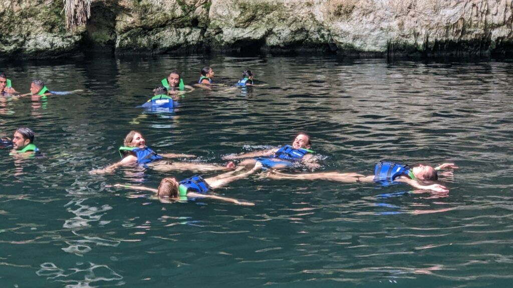 Un groupe de voyageurs WeRoad flotte joyeusement sur le dos dans les eaux calmes d'un cénote mexicain, entouré de parois rocheuses.