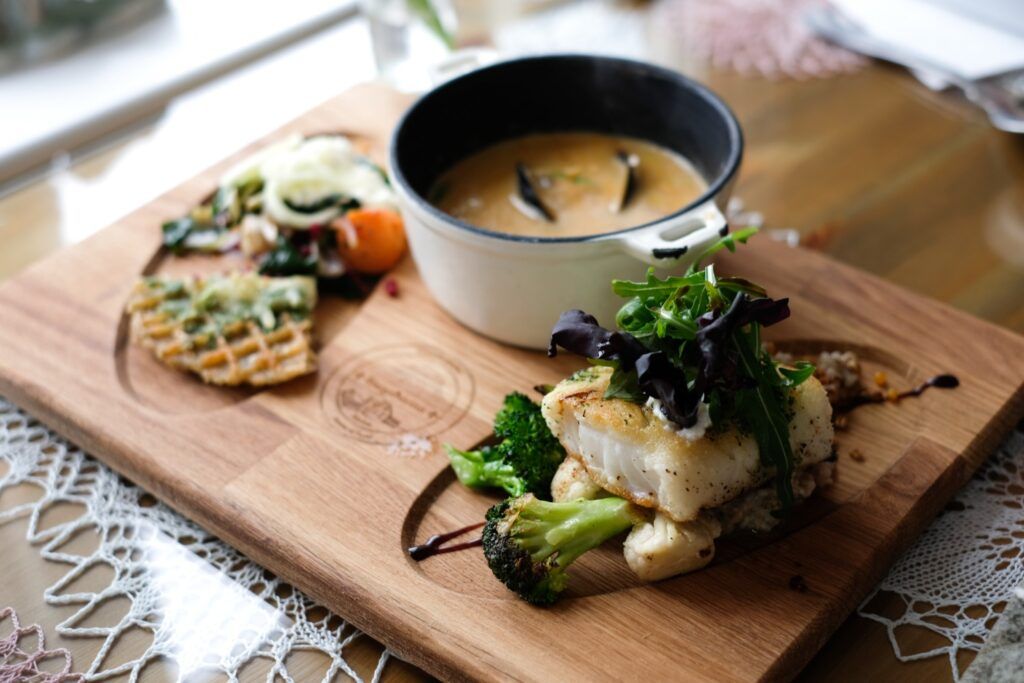 Un plat islandais traditionnel composé d'une soupe crémeuse accompagnée de cabillaud grillé, de brocolis et d'une petite gaufre salée sur une planche en bois.