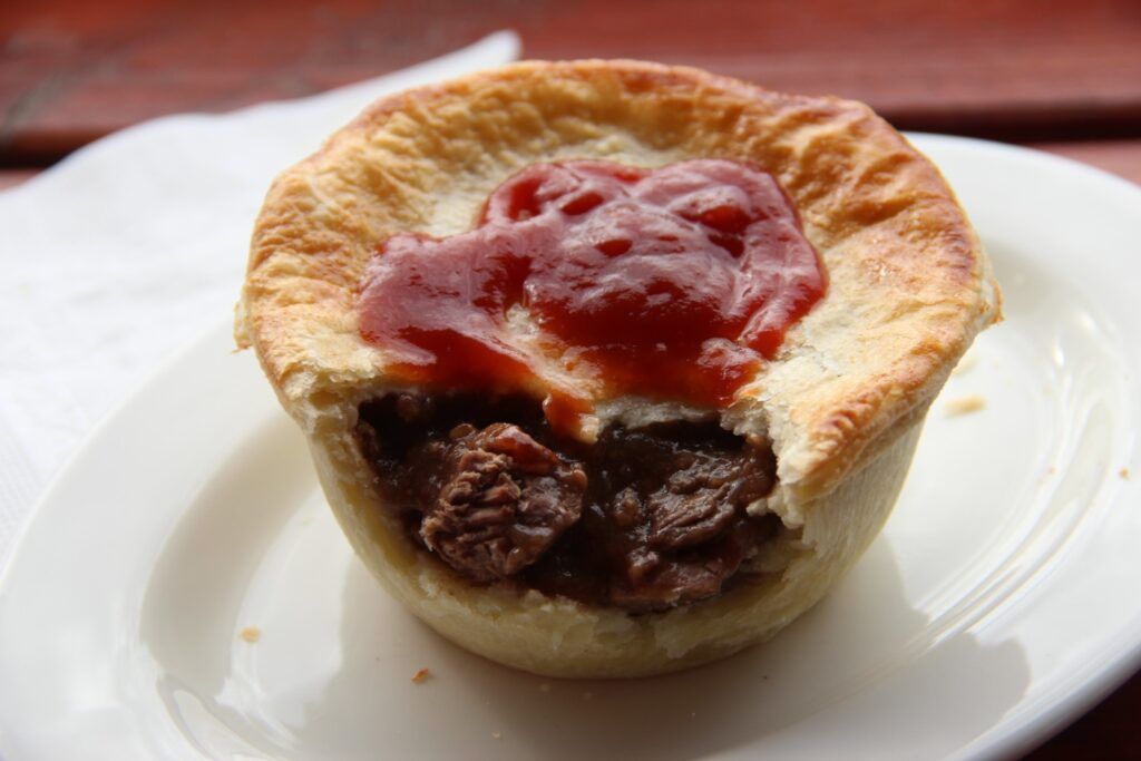 Une tourte à la viande australienne traditionnelle servie sur une assiette blanche et nappée de sauce tomate.