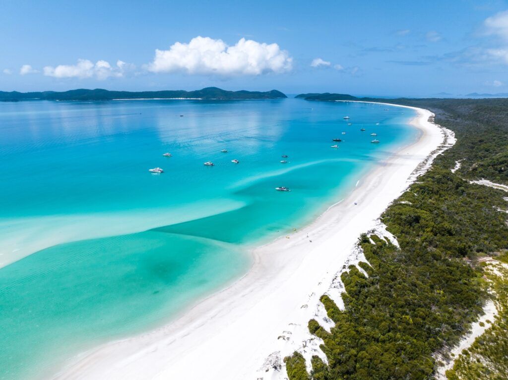 Une vue aérienne de la plage de Whitehaven en Australie, avec son sable blanc éclatant et ses eaux turquoise parsemées de bateaux.