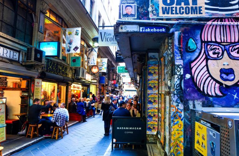 Une ruelle animée de Melbourne avec de l'art urbain coloré, des cafés et des personnes assises aux tables en plein air.