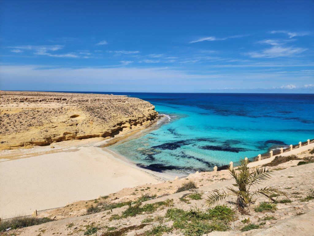 Vue panoramique d'une plage de sable blanc et d'une crique aux eaux turquoise bordée de falaises arides en Égypte.