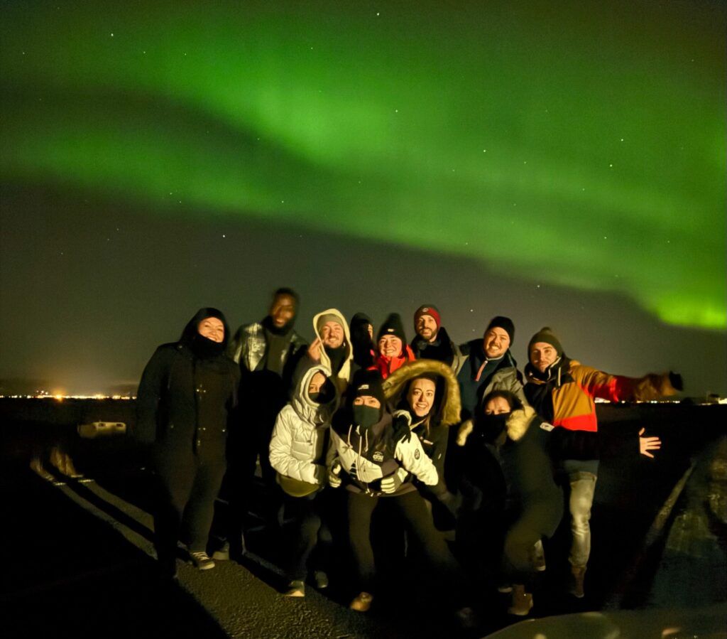 Un groupe de voyageurs WeRoad pose pour une photo de nuit sous une magnifique aurore boréale d'un vert éclatant.