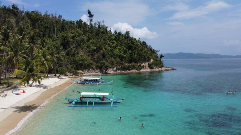 Deux bateaux traditionnels sur les eaux turquoise d'une plage aux Philippines, avec une forêt tropicale dense en arrière-plan.