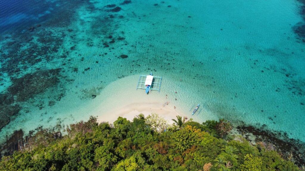 Un bateau traditionnel amarré sur une plage de sable blanc aux eaux cristallines à Palawan, aux Philippines.