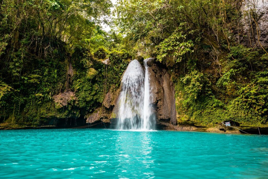 Les chutes de Kawasan aux Philippines, avec une cascade d'eau blanche se déversant dans un bassin turquoise entouré d'une jungle dense.