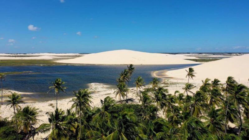 Vue panoramique d’un lagon d’eau douce niché entre d’imposantes dunes de sable blanc et des palmiers verts à Jericoacoara.