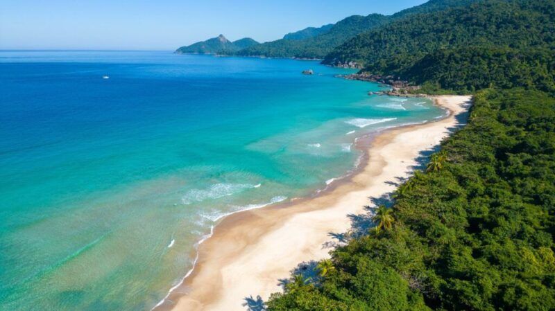 Une vue sur la plage immaculée de Lopes Mendes au Brésil, avec du sable blanc, de l’eau turquoise et une forêt luxuriante.