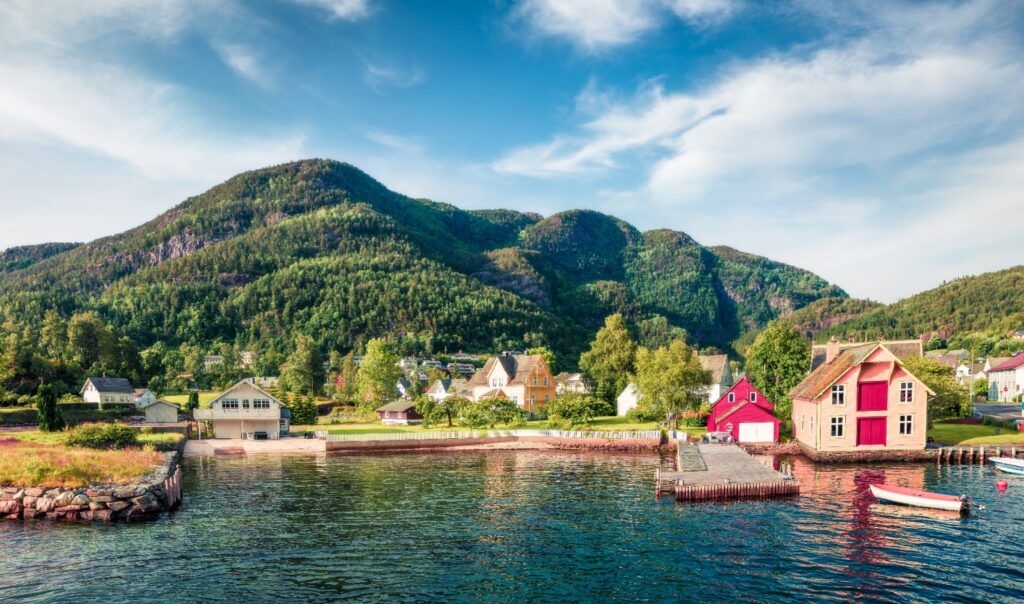 Des maisons norvégiennes colorées au bord d'un lac paisible, entourées de collines verdoyantes sous un ciel bleu d'été.