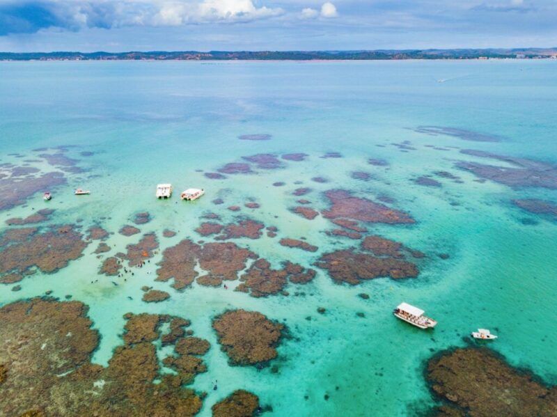 Piscines naturelles de Maragogi montrant des eaux turquoise et des récifs coralliens avec des bateaux.
