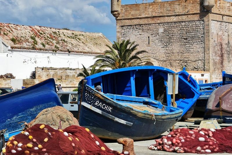 Bateaux de pêche bleus et filets rouges dans le port d'Essaouira, avec la tour de la Skala et les remparts historiques en arrière-plan, Maroc