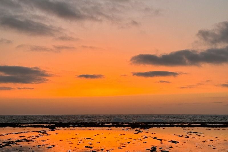 Coucher de soleil orangé sur une côte rocheuse avec des flaques d'eau reflétant le ciel embrasé au-dessus de l'océan