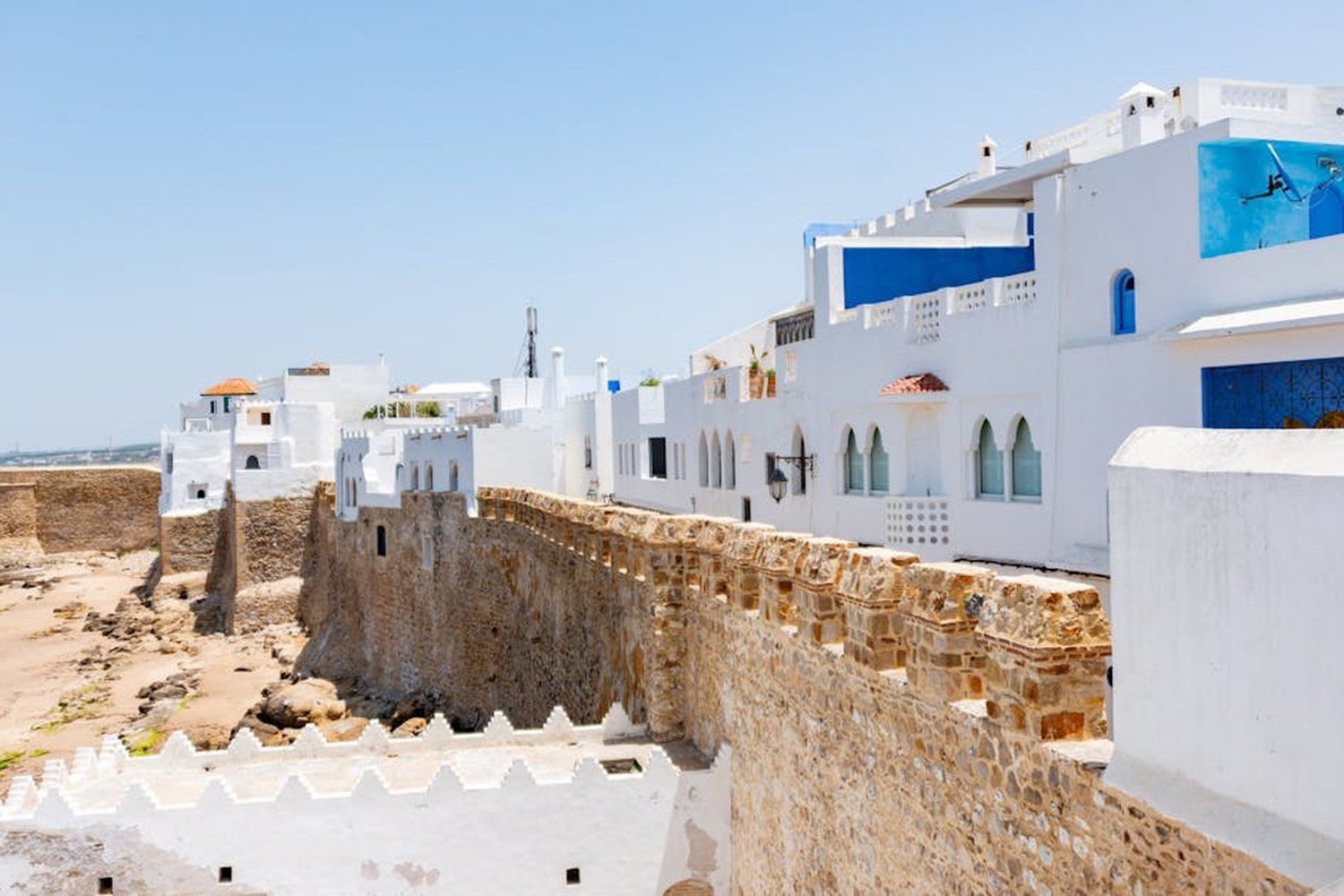 Remparts en pierre dorée d'Asilah avec les maisons blanches et bleues de la médina surplombant la plage, au Maroc