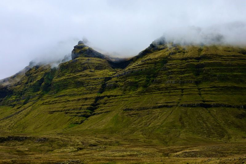 Montagnes vertes aux strates basaltiques enveloppées de nuages bas sur un paysage Islande