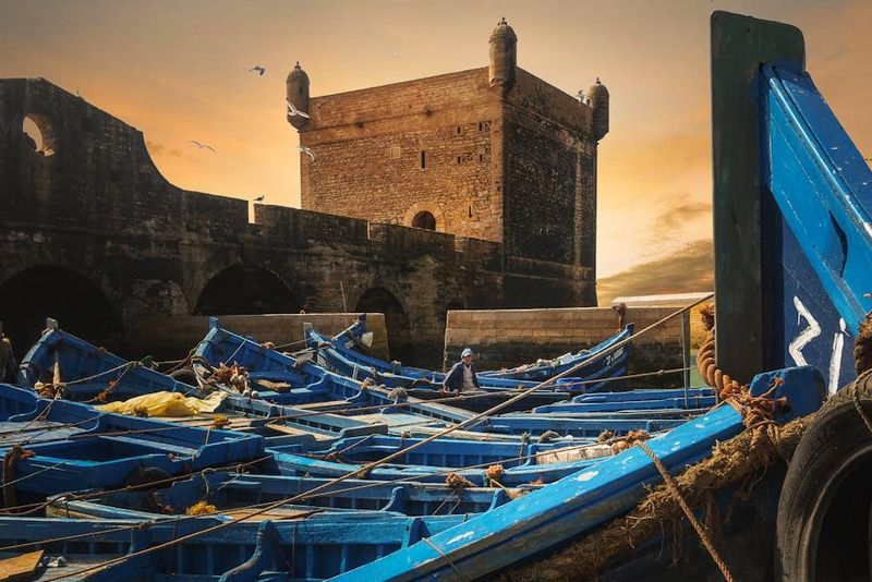 Dizaines de bateaux de pêche bleus amarrés dans le port d'Essaouira devant la forteresse Skala du Port au coucher du soleil, Maroc
