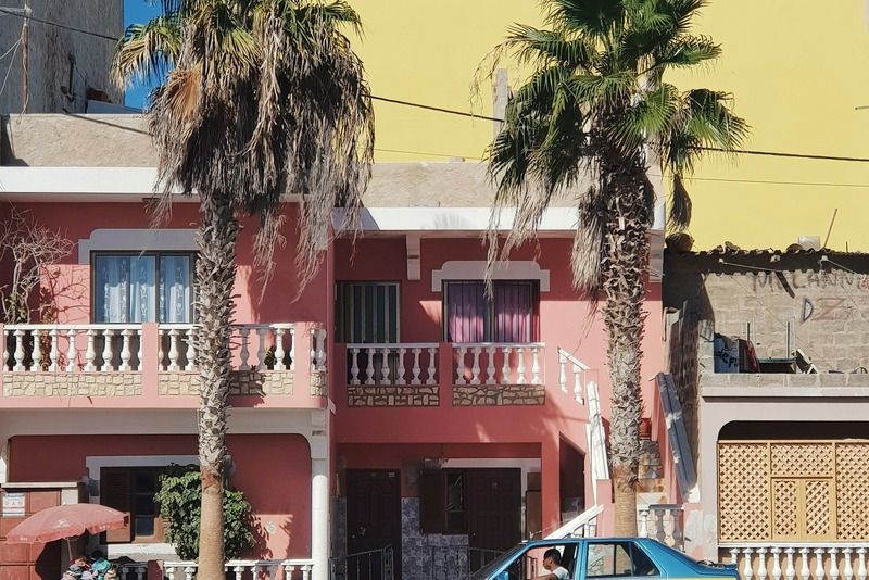 Taxi jaune et bleu garé dans une rue ensoleillée devant des maisons roses et jaunes ornées de grands palmiers