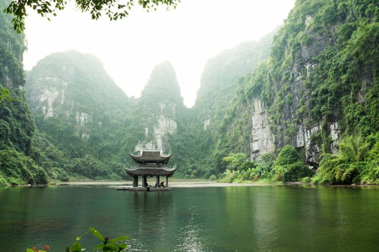 Pagode traditionnelle au milieu du lac de Trang An, entourée de falaises calcaires couvertes de végétation tropicale, Ninh Binh, Vietnam