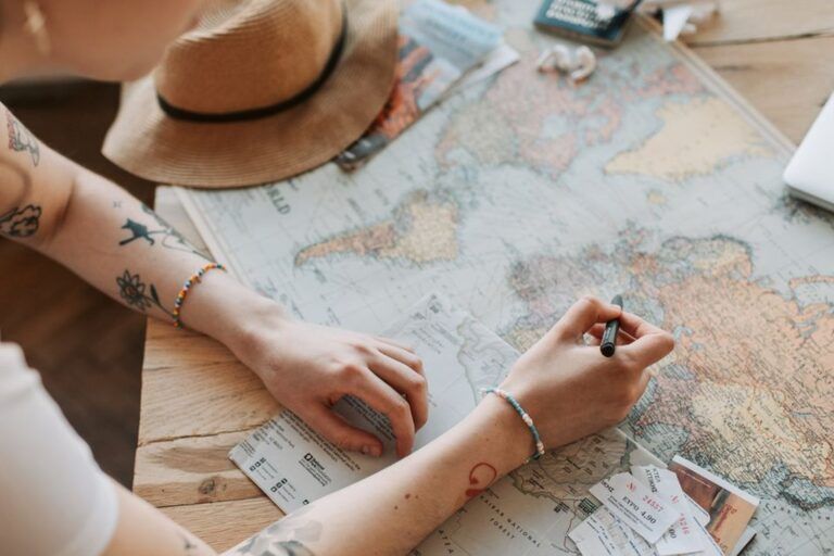 Femme tatouée penchée sur une carte du monde avec des billets de voyage et un chapeau de paille, planifiant son prochain voyage