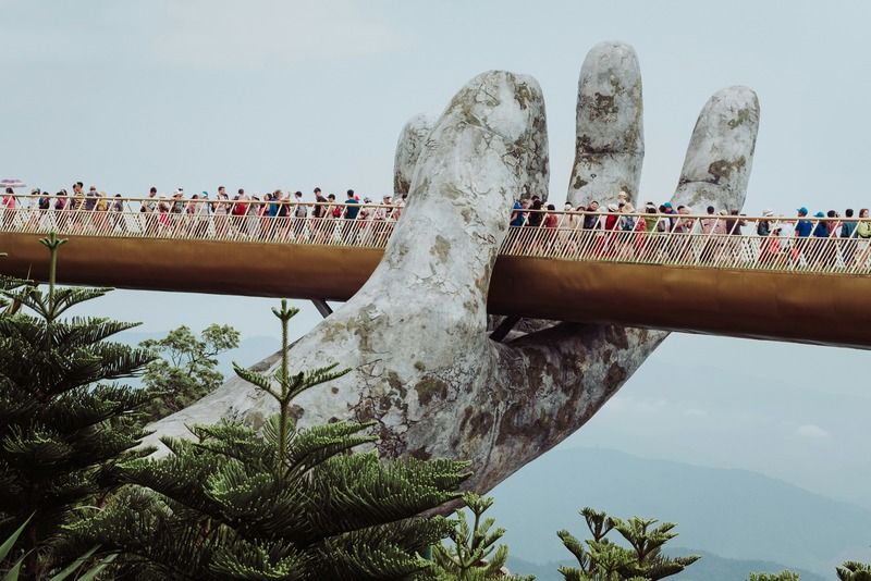 Le Pont d'Or de Ba Na Hills soutenu par deux mains géantes en pierre, avec des visiteurs qui se promènent au-dessus de la forêt de pins, Vietnam