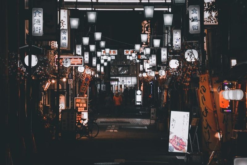 Ruelle animée illuminée par des lanternes et des enseignes de restaurants japonais la nuit, avec des inscriptions en kanji
