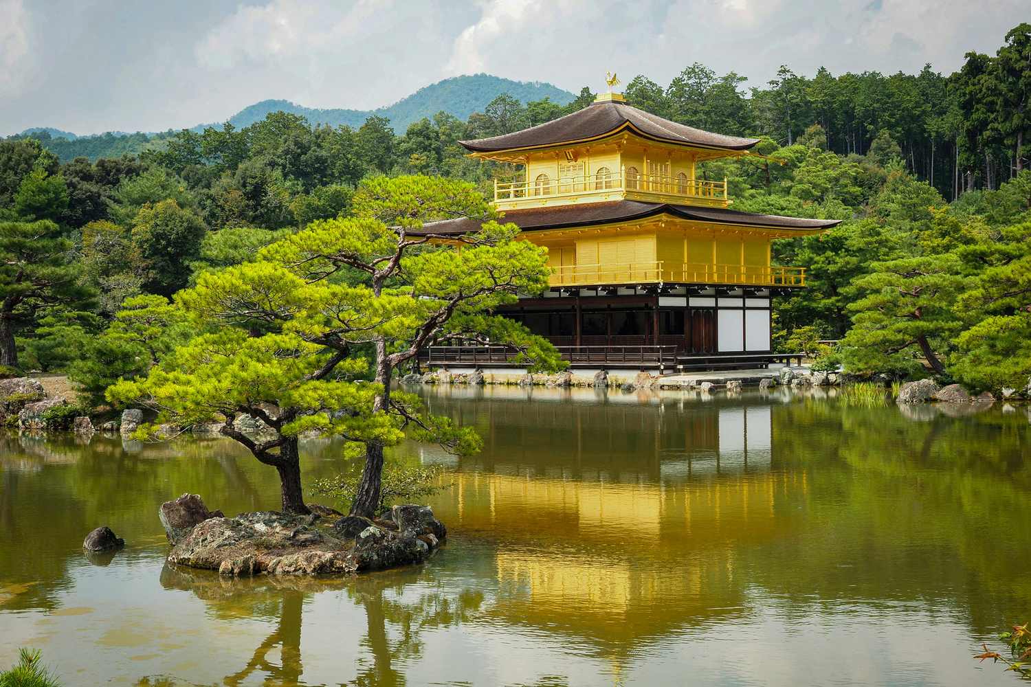 Le Pavillon d'Or (Kinkaku-ji) reflété dans l'étang du jardin de Rokuon-ji, entouré d'arbres et de montagnes verdoyantes à Kyoto, Japon