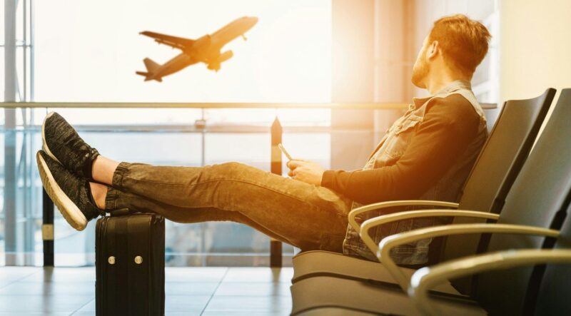 Voyageur assis dans un aéroport avec une valise, regardant un avion décoller par la fenêtre