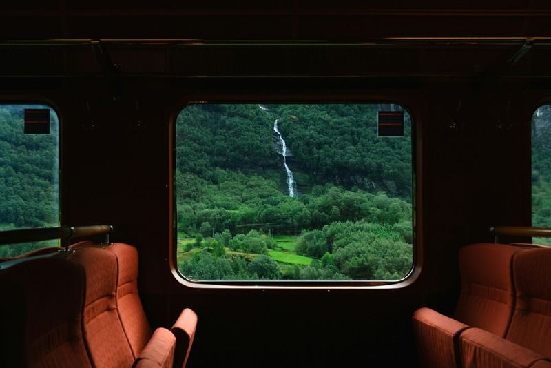 Vue depuis la fenêtre d'un train sur une cascade entourée de forêts verdoyantes et de montagnes