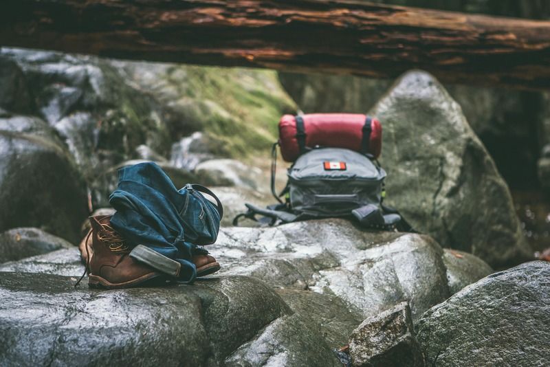 Chaussures de randonnée, jean retroussé et sac à dos de camping posés sur des rochers en forêt