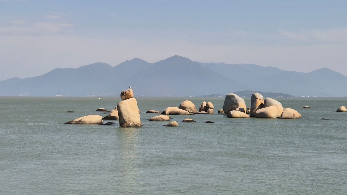 Gros rochers dans une mer calme avec montagnes lointaines sous un ciel clair