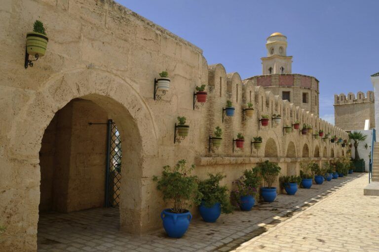 Passage voûté en pierre de la médina de Hammamet, orné de pots colorés, avec une tour à coupole en arrière-plan