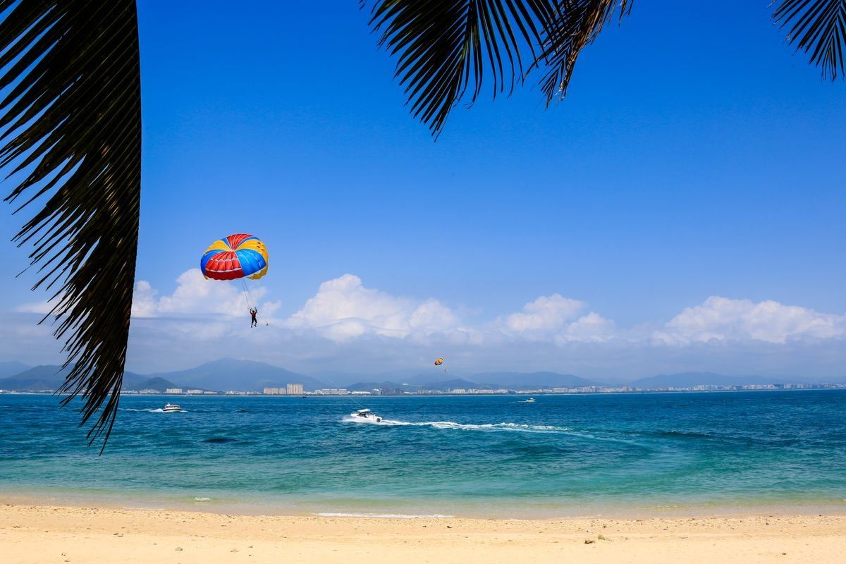 Parachute ascensionnel au-dessus de la mer, plage de sable et palmes au premier plan