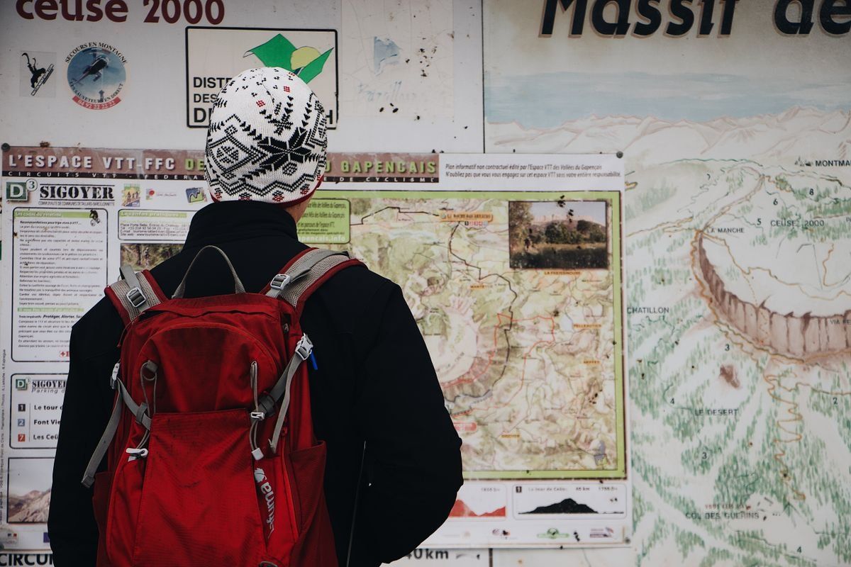 Personne avec sac à dos rouge devant un panneau de cartes de randonnée