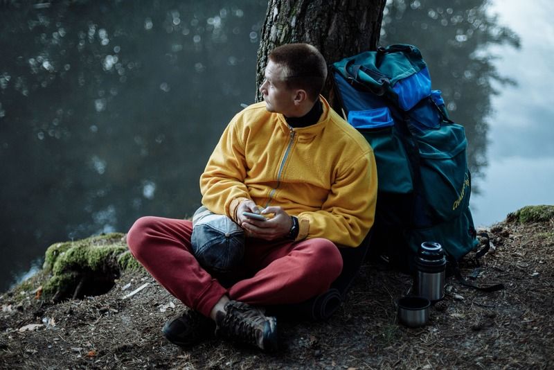 Randonneur en pause au bord d'un lac avec un sac à dos et un thermos pendant une randonnée