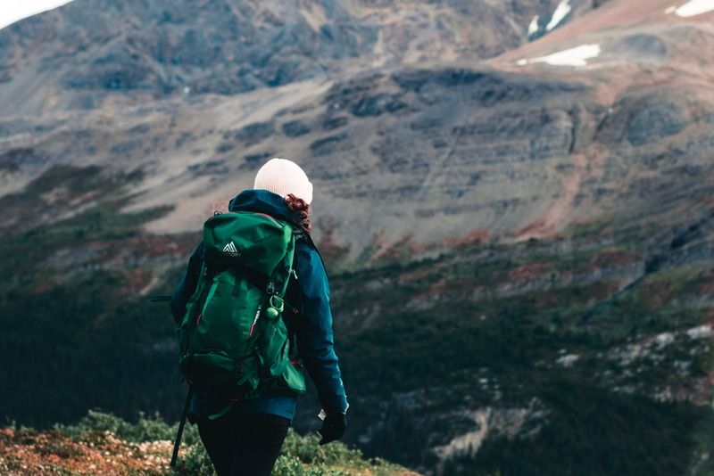 Randonneuse avec un sac à dos vert marchant sur un sentier de montagne vers un sommet rocheux