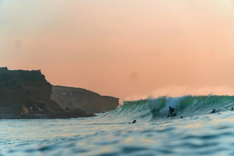 Surfeur au sommet d'une vague au coucher du soleil, avec des falaises en silhouette sur la côte portugaise