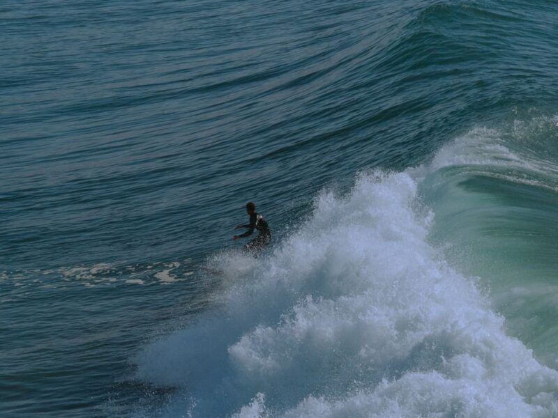 Surfeur au milieu de l’écume sur une vague vue de loin.