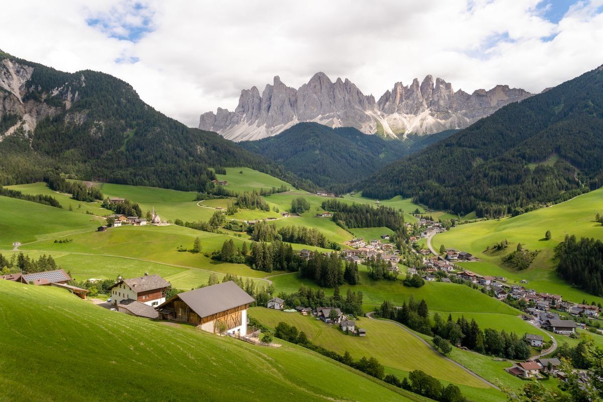 Vallée verdoyante avec fermes, village et route sinueuse sous des sommets dentelés