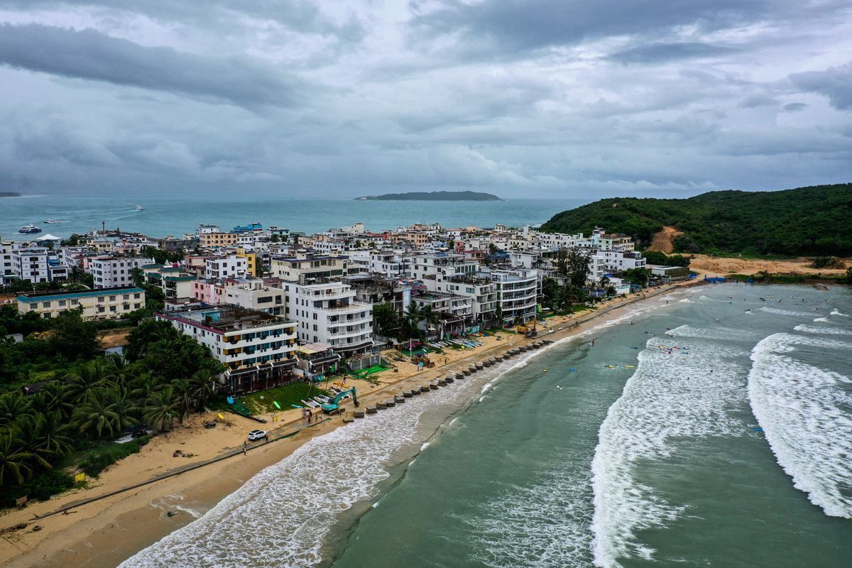 Vue aérienne d’une ville côtière bordée par une plage et des vagues sous un ciel nuageux