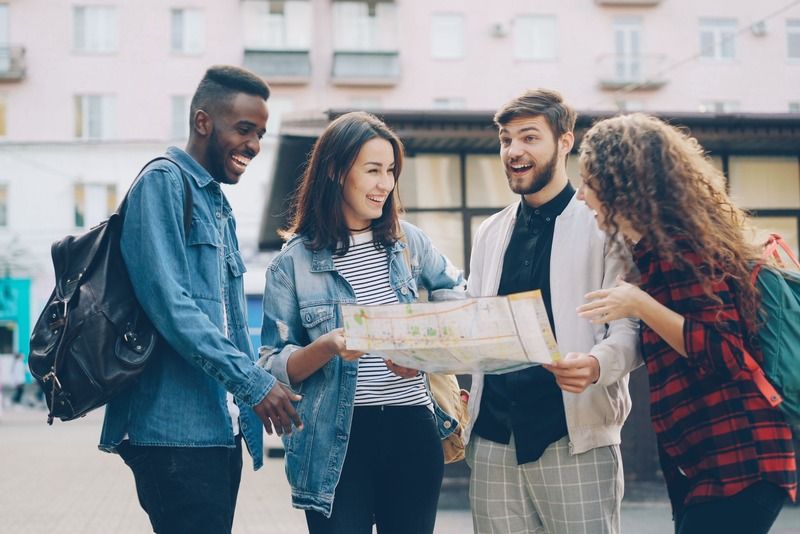 Quatre amis riant en consultant une carte papier dans une rue de ville aux façades pastel