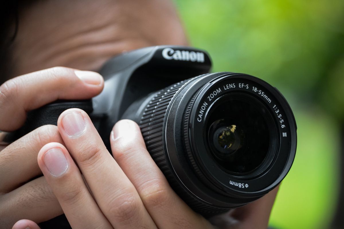 Gros plan sur des mains tenant un appareil photo Canon avec objectif zoom