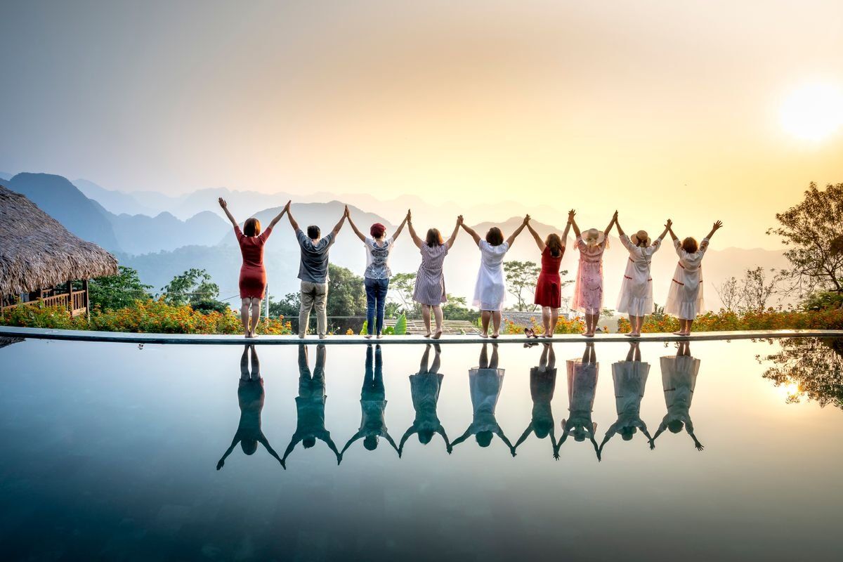 Groupe d’amis levant les bras devant un lac au coucher du soleil