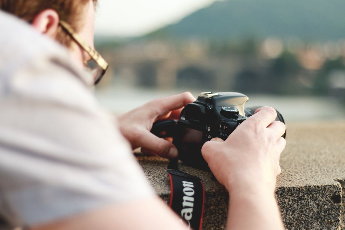 Personne appuyée sur un muret tenant un appareil photo reflex en extérieur