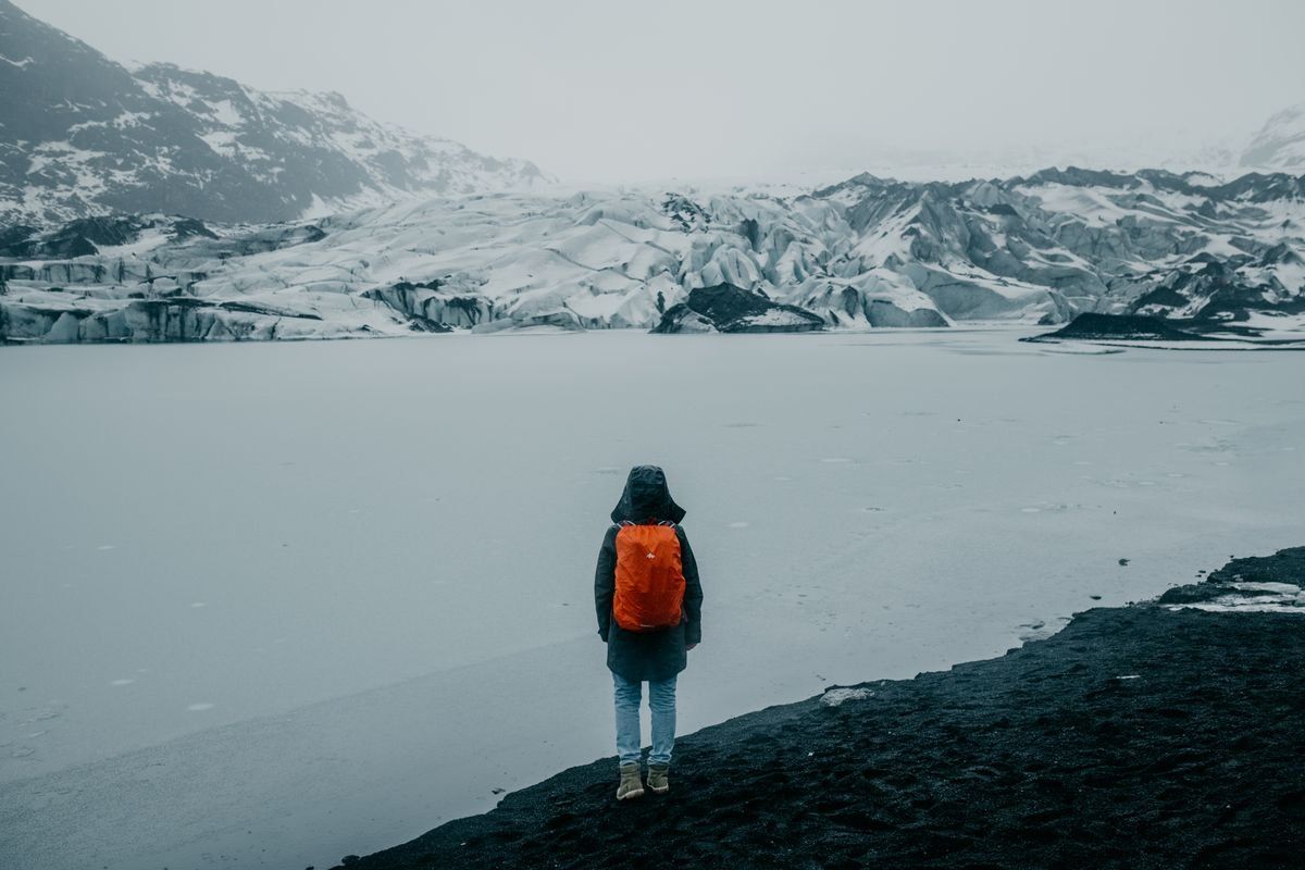 Personne avec sac à dos orange face à un paysage enneigé et glacé