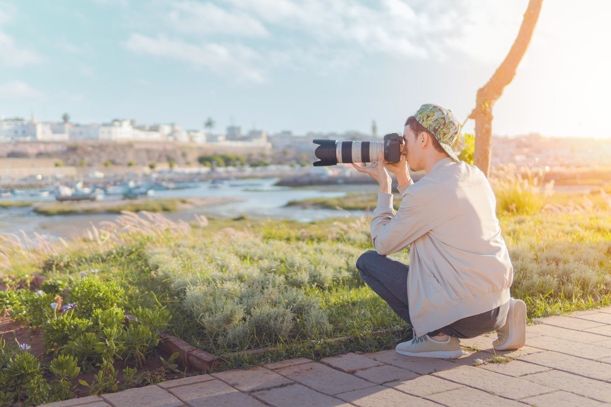 Photographe accroupi avec téléobjectif face à un paysage côtier ensoleillé