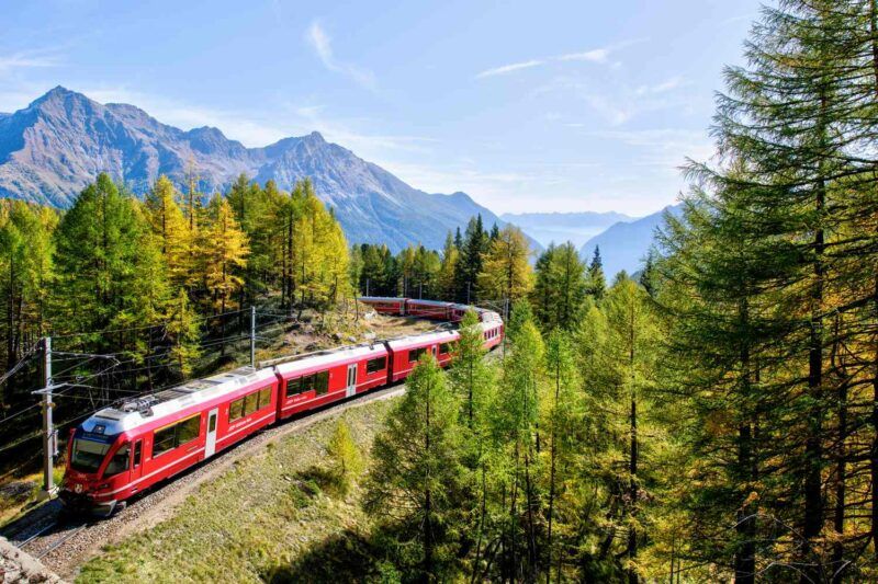 Train rouge à voie étroite traversant une forêt de mélèzes dorés dans les Alpes suisses