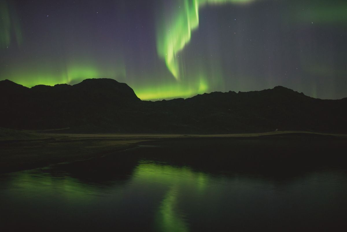 Aurores boréales vertes au-dessus de montagnes sombres reflétées dans un lac calme